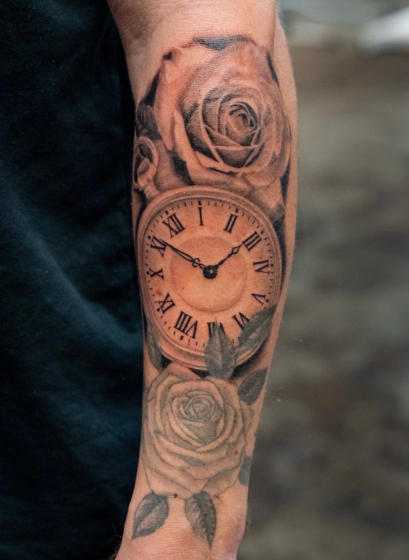 Tattoo of a pocket watch with roses on a person's arm, shaded in black and gray.