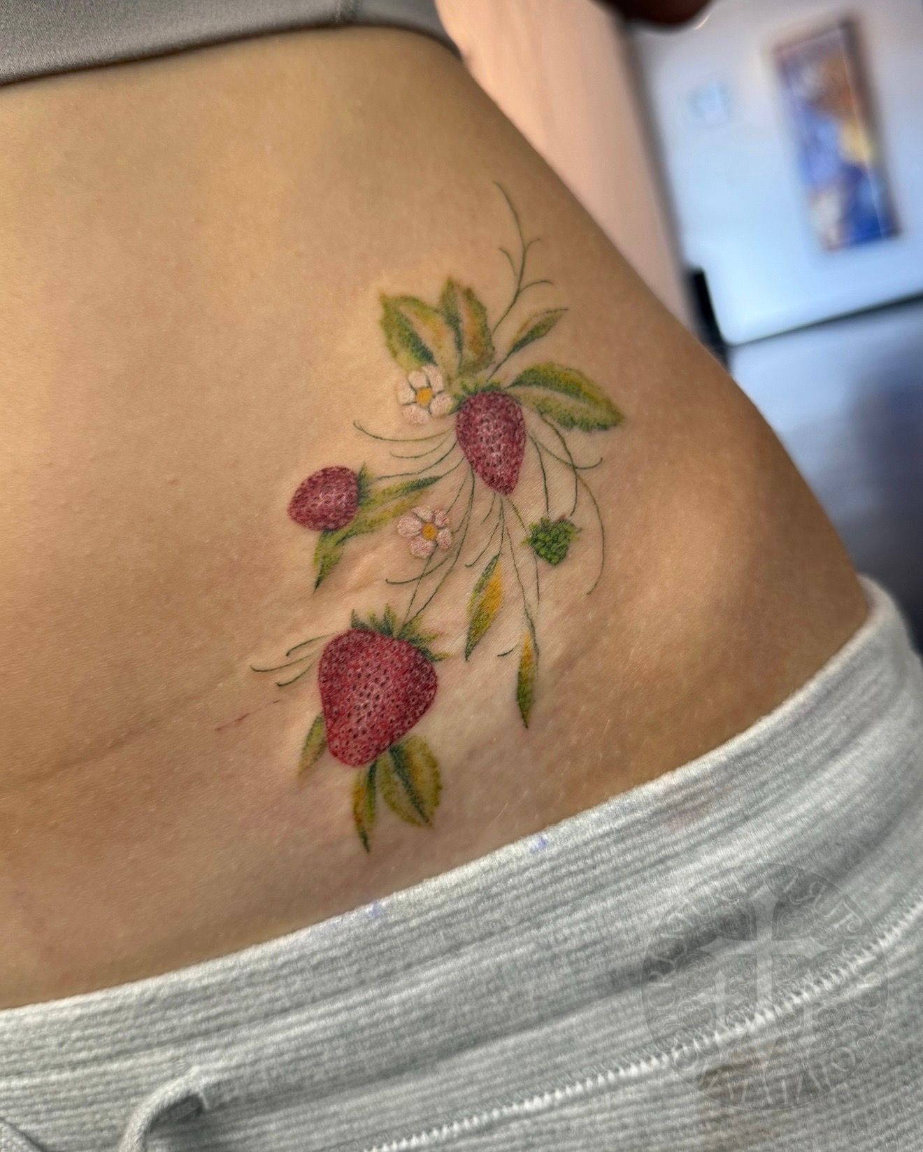 Strawberry tattoo on a person's side, featuring red berries, green leaves, and delicate stems.