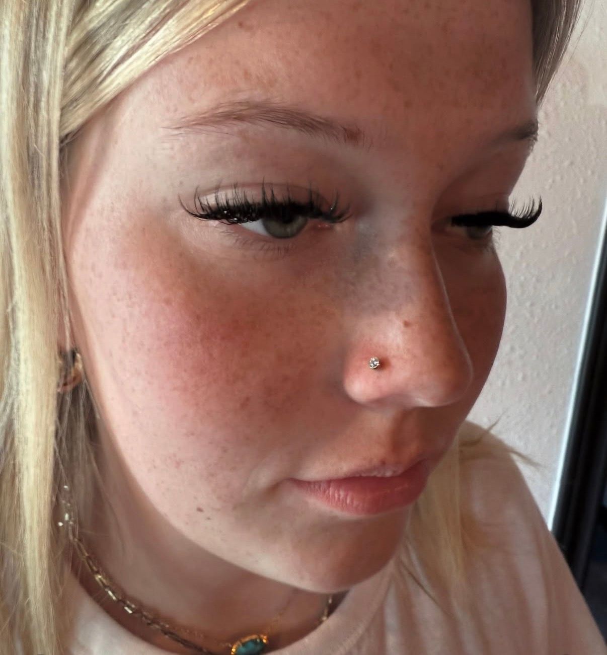 Woman with a nose piercing, long eyelashes, and fair skin, looking down.