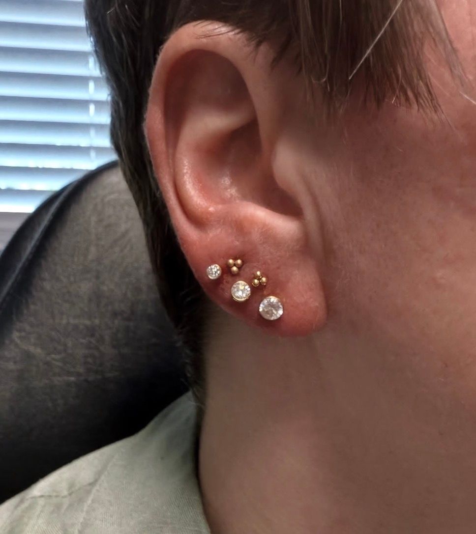 Ear with multiple piercings, each holding a stud earring with a gemstone.