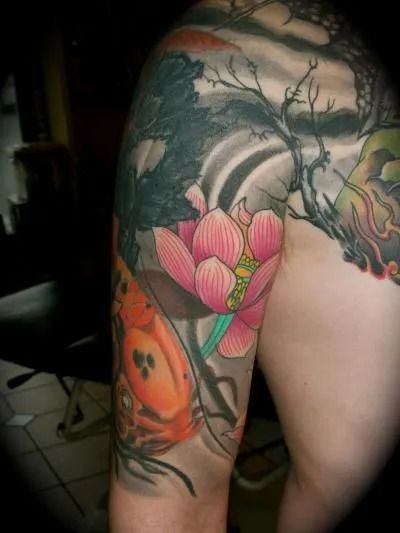 Tattoo on an arm with a lotus flower, koi fish, and Japanese-style landscape in pink, orange, gray, and black.