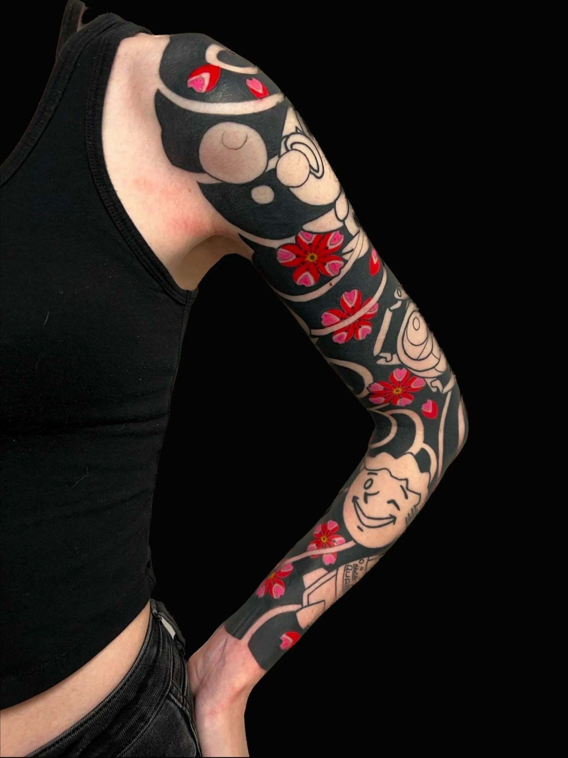 Person's arm with black tattoo sleeve, featuring white faces, red flowers, and black shapes.