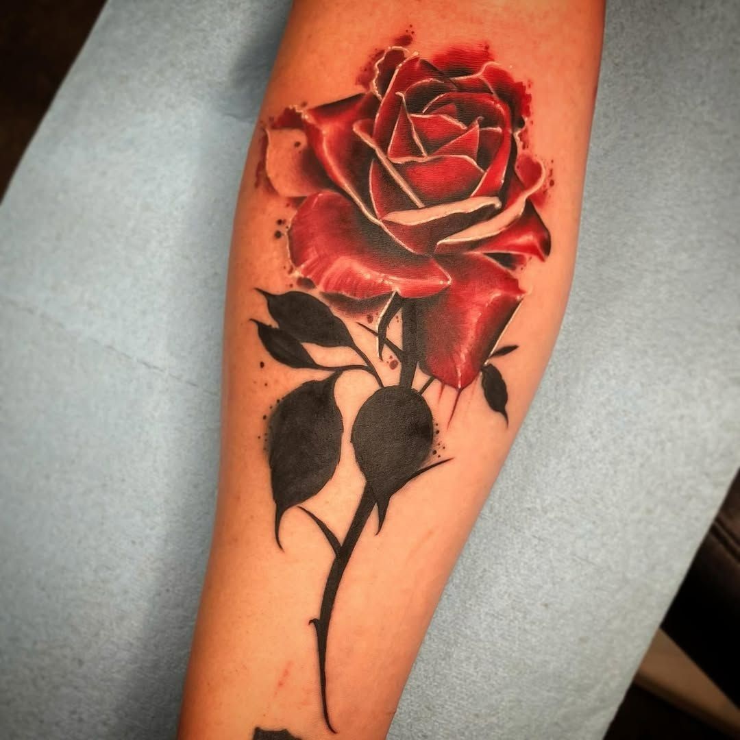A red rose tattoo with black stem and leaves on a forearm.