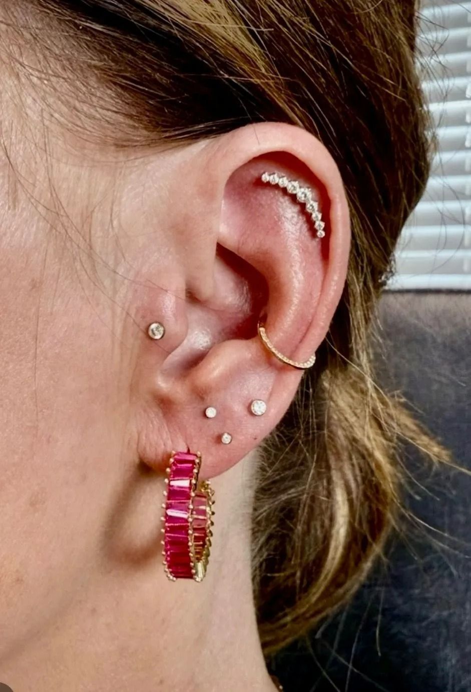 Close-up of ear with multiple piercings, including hoop earrings and a curved helix bar.