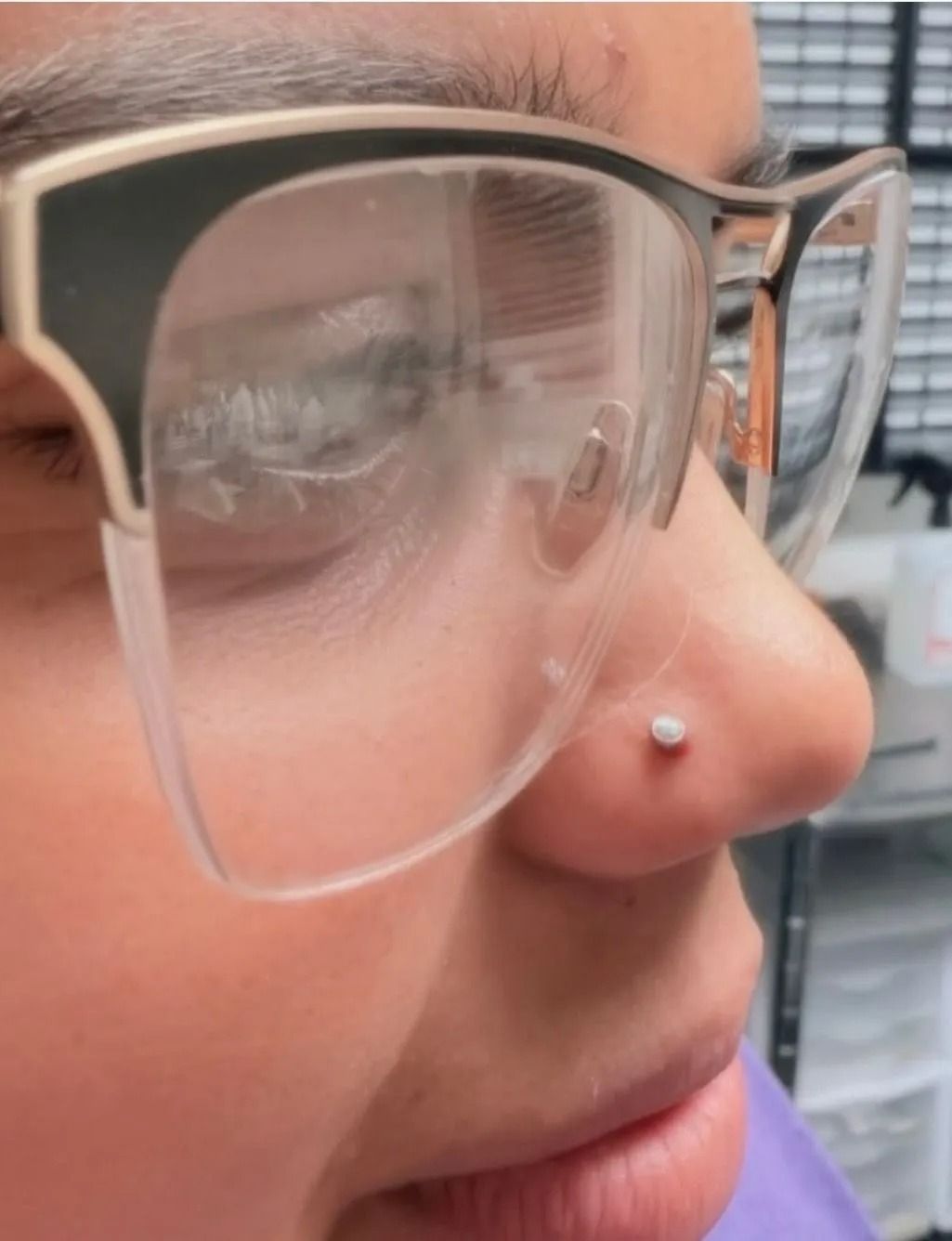 Person wearing glasses, nose pierced with small stud.