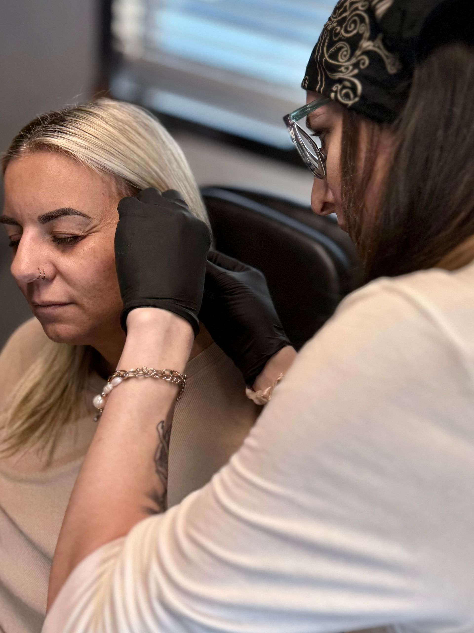 A practitioner wearing black gloves performs a cosmetic procedure on a client's ear in a professional setting.
