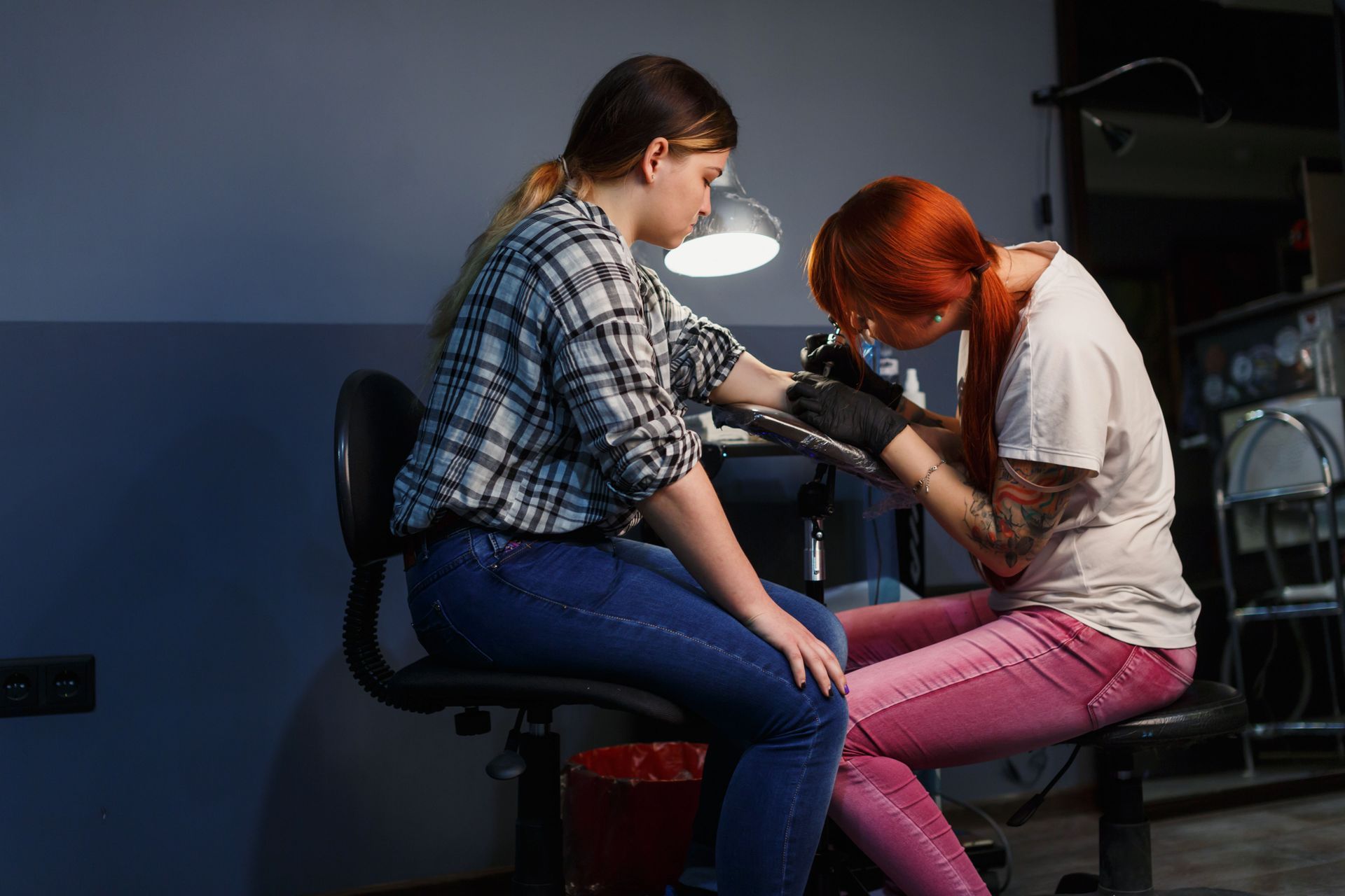 A person with red hair tattoos a person's arm in a tattoo studio.