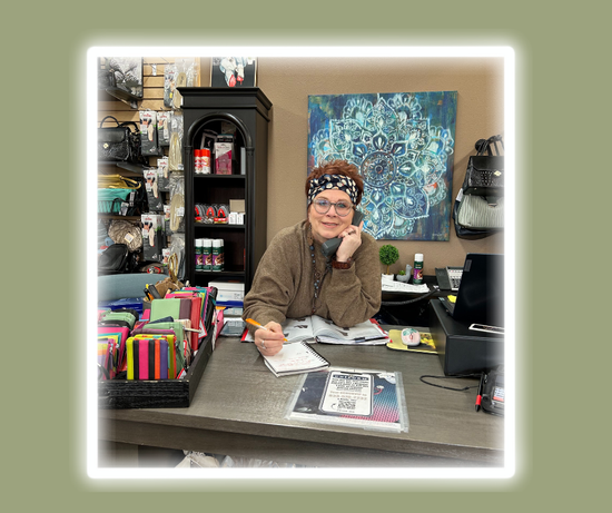 Britta Burbach sits at a desk in front of a painting that says ' mandala ' on it