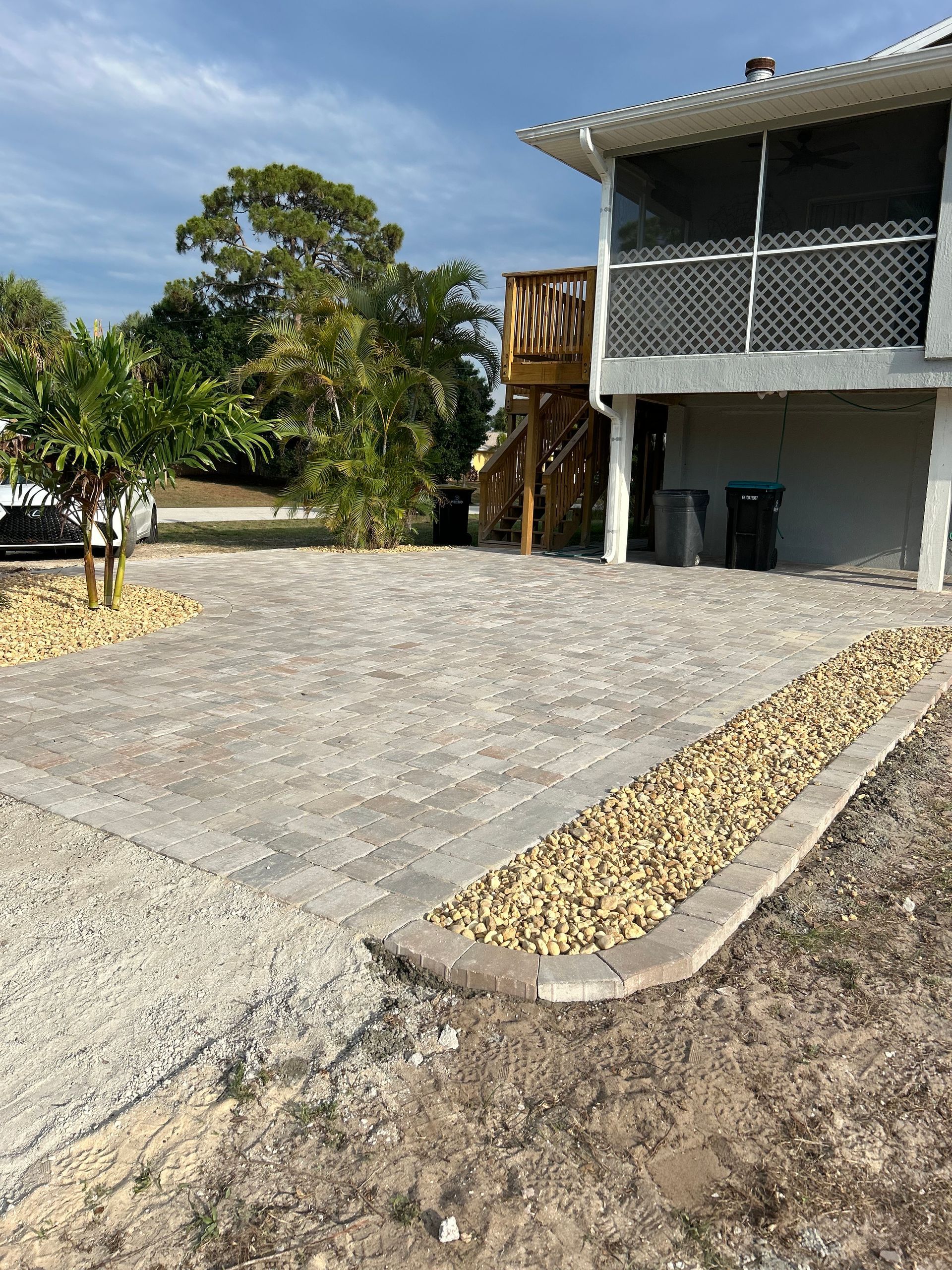 A house with a screened in porch and a gravel driveway in front of it.