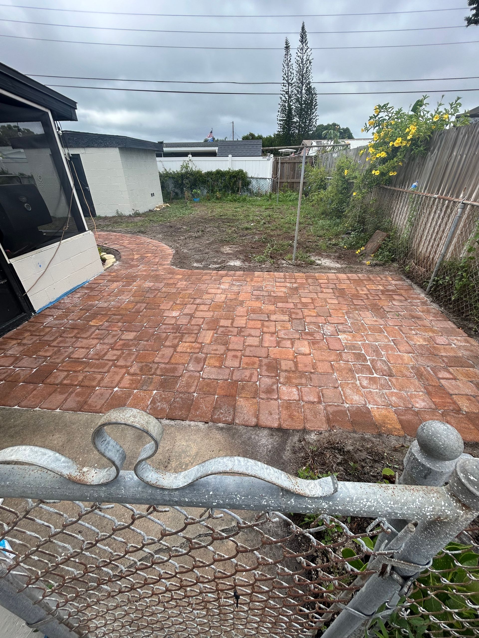 A chain link fence surrounds a brick walkway in a backyard.