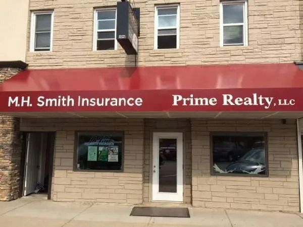 A brick building with a red awning. Text reads "M.H. Smith Insurance Prime Realty, LLC".