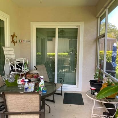 Covered patio with glass sliding door, outdoor table, chairs, and potted plants.