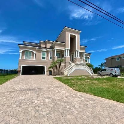Large modern beige house with a driveway, front stairs, and a blue sky with power lines overhead