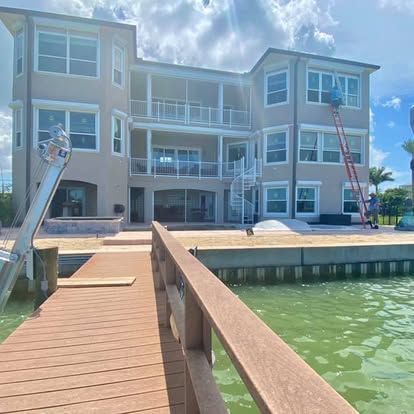 Waterfront condo building with dock and walkway over green water under a bright blue sky