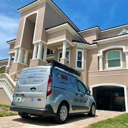 Work van parked in front of a large tan house with a garage and blue sky.