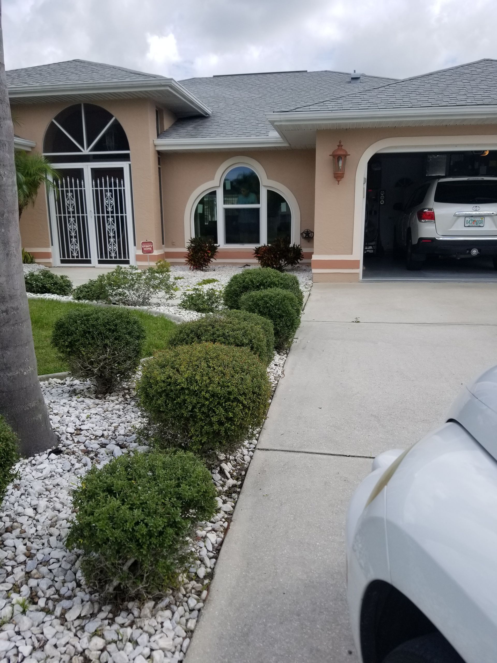 Suburban house front with driveway, trimmed shrubs, and a car parked in the garage