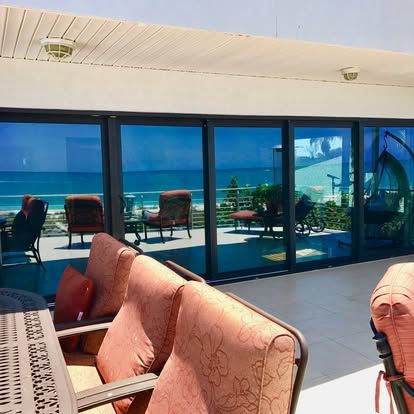 Outdoor patio with pink chairs overlooking a blue ocean and distant mountains through glass doors