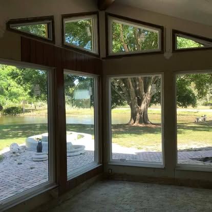 Interior view through large windows of a lakeside room, showing a patio and trees outside.