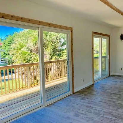 Bright empty room with sliding glass doors opening to a wooden deck and tropical yard