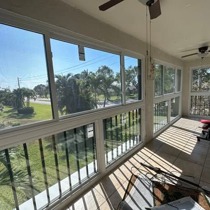 Sunny screened porch overlooking a green lawn and palm trees, with white railings and hanging ceiling fans.