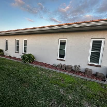 Long beige house wall with small windows, grass lawn, and landscaped rocks at dusk