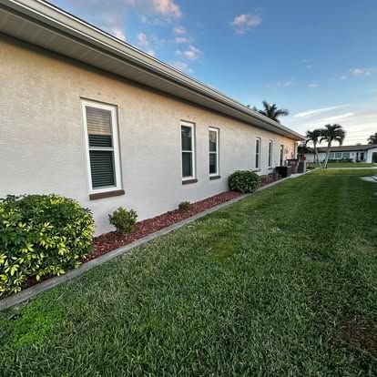 Single-story beige house with white windows, red mulch, and a green lawn under a blue sky.