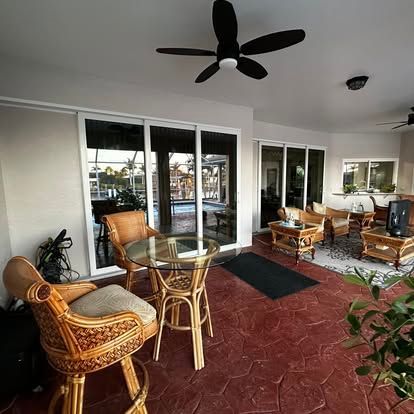 Covered patio with wicker seating, glass table, red tile floor, and ceiling fan facing a pool.