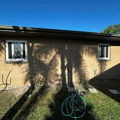 Tan stucco house exterior with two windows, blue sky, and a green garden hose in the foreground