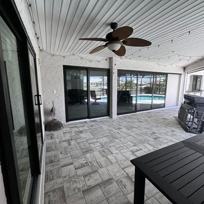 Covered patio with gray pavers, ceiling fan, sliding glass doors, and a pool view beyond the railing