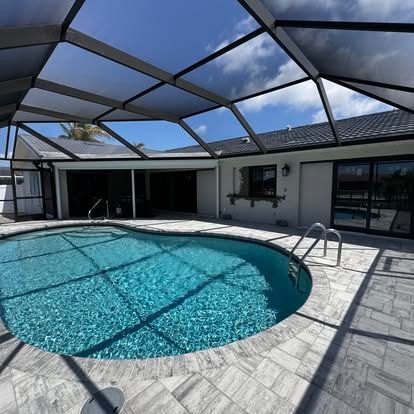 Screened backyard pool with light stone patio and blue sky overhead