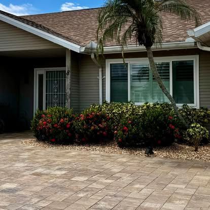 Suburban house with palm tree, tiled driveway, and flowering shrubs under a partly cloudy sky