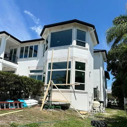 Two-story white house with large windows and ladders under blue sky, mid-renovation