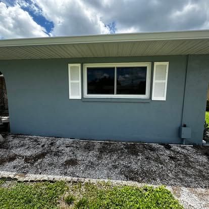 Blue-gray house exterior with a single window and white shutters under a cloudy sky