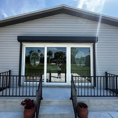 Front view of a small white building with double glass doors, steps, railings, and potted flowers