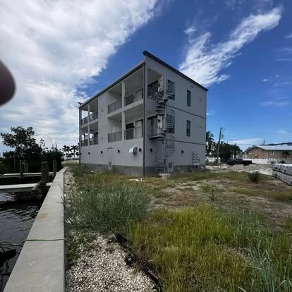 Three-story gray apartment building beside a canal under a blue sky