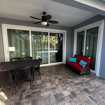 Covered patio with wicker dining set, red-cushioned sofa, ceiling fan, and sliding glass doors.