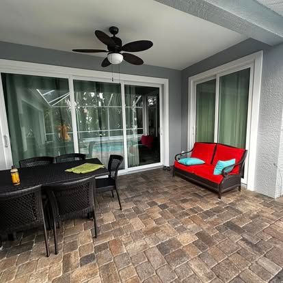 Covered patio with brick pavers, black dining set, red bench, and sliding glass doors