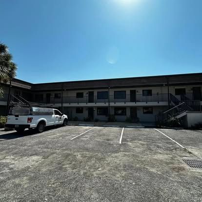 Motel-style two-story building with a white pickup truck parked in a sunlit lot under a clear blue sky