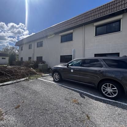 Dark SUV parked beside a beige two-story building under a bright cloudy sky