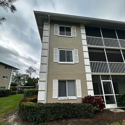 Three-story beige apartment building with white trim, balconies, and cloudy sky.