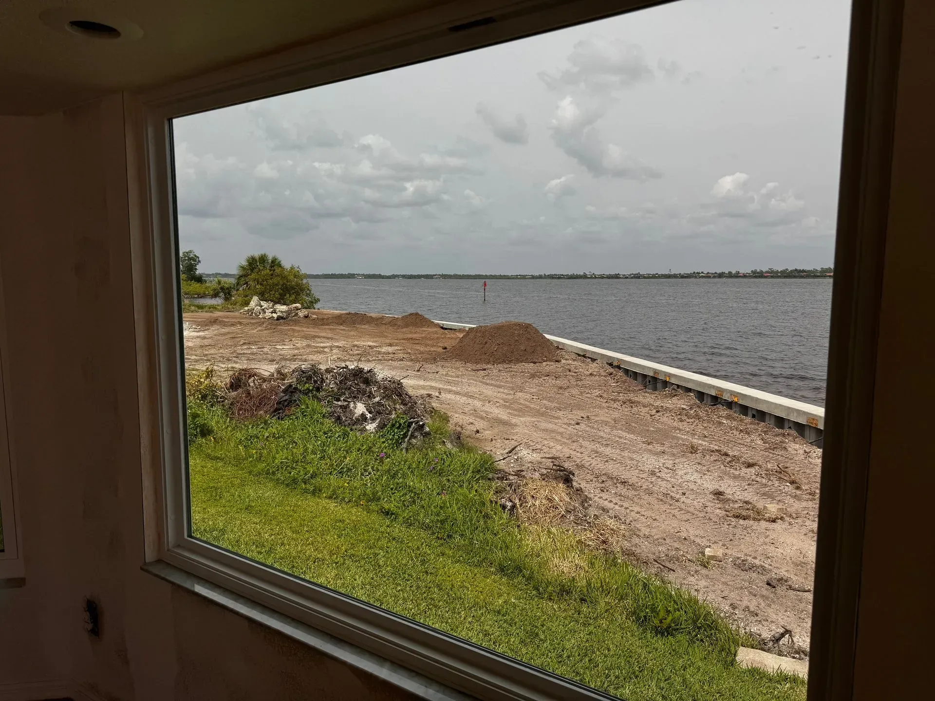 View through a window of a rocky shoreline and calm water under a cloudy sky.