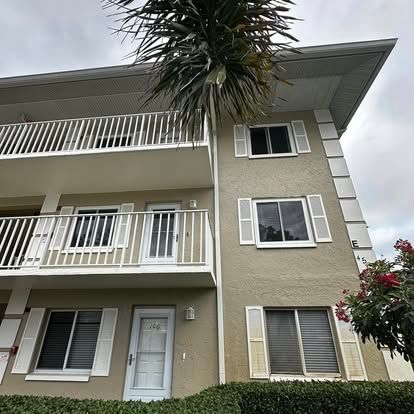 Three-story beige apartment building with white balconies and a palm tree in front