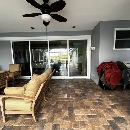 Covered patio with wicker chairs, ceiling fan, sliding glass doors, and a red grill cover on tiled floor