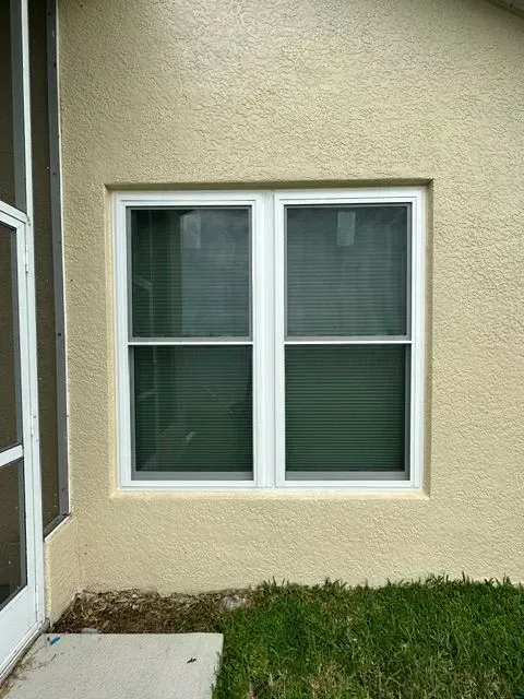 Small white-framed window in a beige stucco wall beside a door and grass.