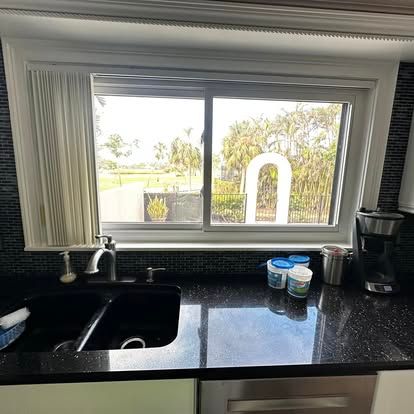 Kitchen sink and black countertop beneath a bright window overlooking a yard and white archway.