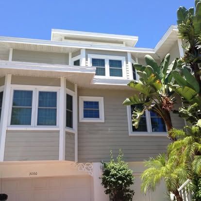 Modern beige house exterior with white trim, blue windows, and tropical palm trees in front
