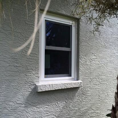 White-framed window on a textured gray stucco wall, with tree branches overhead.