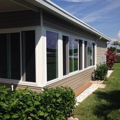 Modern house exterior with large windows, beige siding, and green shrubs along a sunny lawn