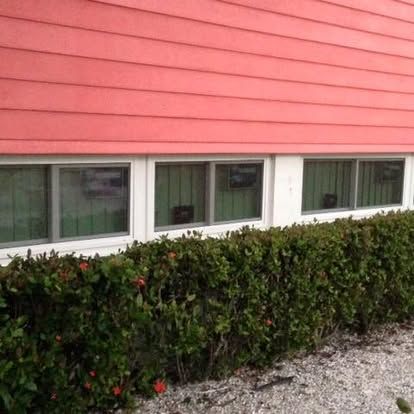 Pink house exterior with three windows above a neatly trimmed hedge and gravel foreground