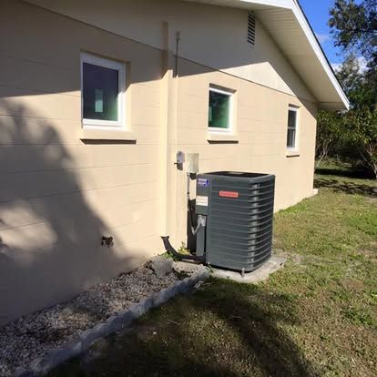 Side view of a beige house with two windows and a gray outdoor air conditioner unit beside the wall.